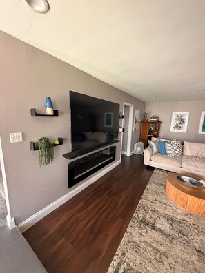 Ein Wohnzimmer mit flachbildfernseher an der Wand, einem Holztisch und einem beigefarbenen Sofa.