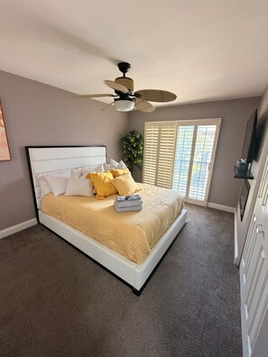 Ein Schlafzimmer mit einem Bett, einem Deckenventilator, einem Fenster mit Jalousien und einer Pflanze.