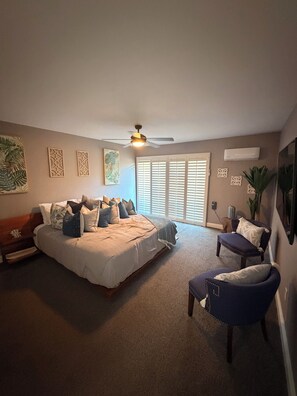 A bedroom with a large bed, a ceiling fan, a window with blinds, and a small table with a chair. - Solana Beach Coastal Townhouse (Solana Beach)
