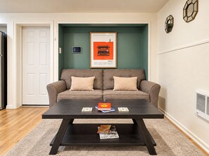 Ein Wohnzimmer mit einem dunklen Holztisch, einem beigefarbenen Sofa mit zwei Kissen und einem gerahmten Poster an der Wand.