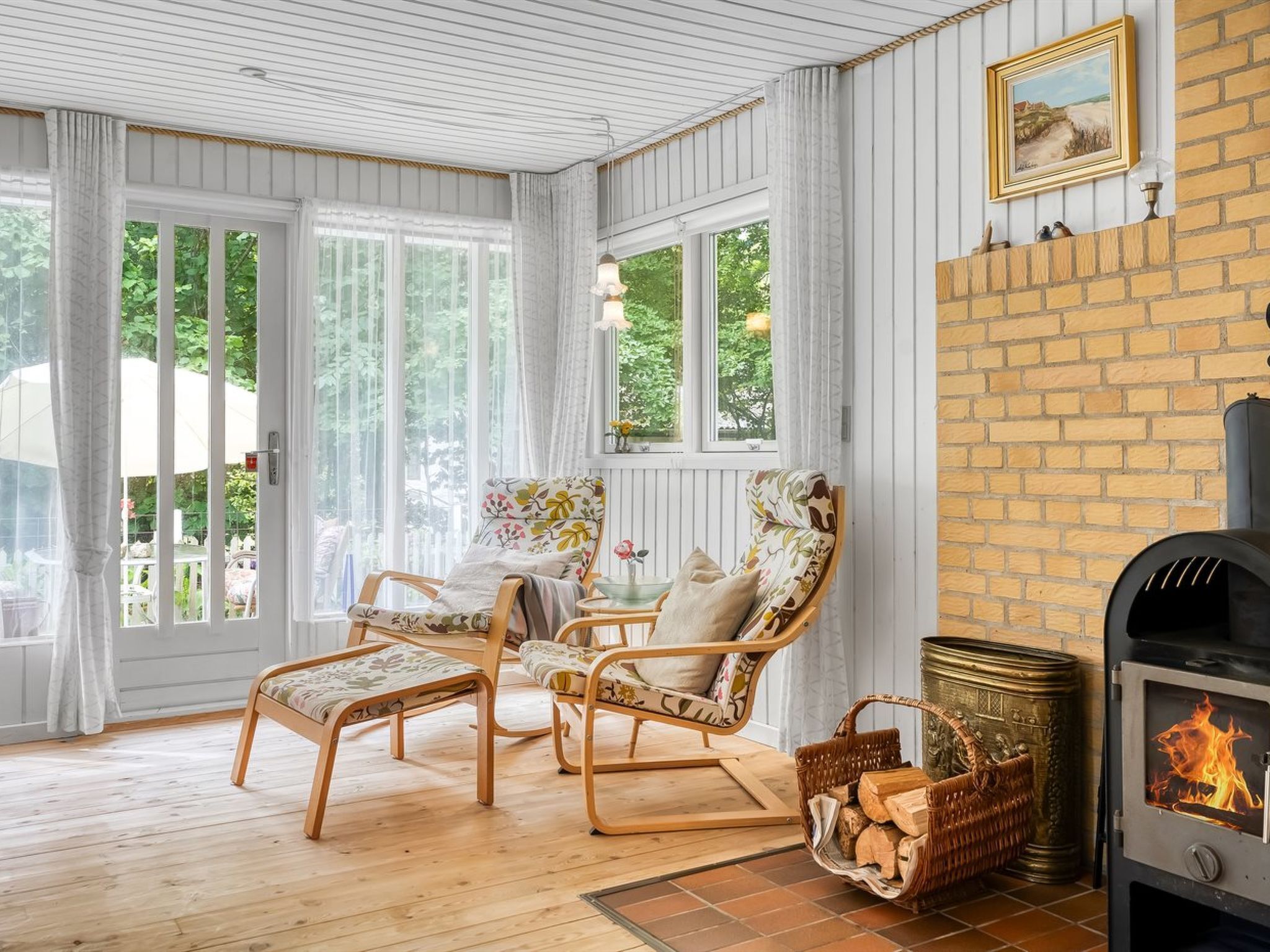 Een kamer met een open haard, houten vloeren en grote ramen voorzien van gordijnen.