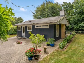 Ein kleines, dunkel gefärbtes Haus mit einem Ziegeldach, einer Haustür und einem Schornstein. Blumentöpfe und ein kleiner Garten mit einem Weg zum Haus.