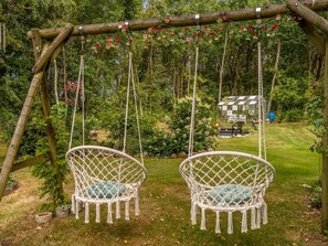 Ein Garten mit zwei weißen Korbschaukelstühlen unter einer hölzernen Pergola mit Blumen.