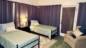 A room with two beds, a chair, a ceiling fan, and a door.