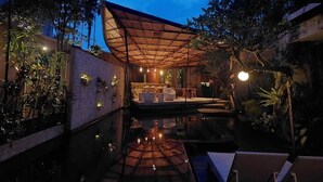 An outdoor pool area with a covered seating area, surrounded by plants and trees. - Dewi Resort Ubud  (Ubud)