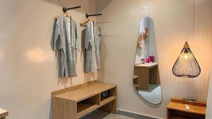 Una habitación con un banco de madera, un espejo y un perchero con prendas estampadas.