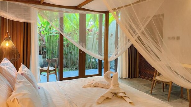 A bedroom with a bed, a chair, and a view of greenery outside. - Dewi Resort Ubud  (Ubud)