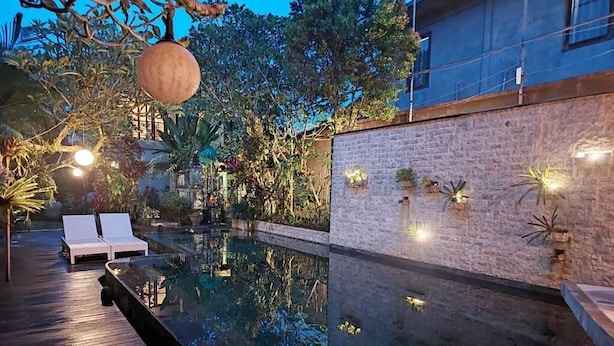 Una piscina con cubierta de madera, rodeada de plantas y un muro de ladrillo.