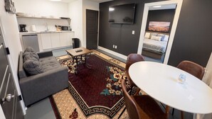 Un espacio habitable compacto con kitchenette, un sofá, una mesa de comedor y un televisor montado en la pared.