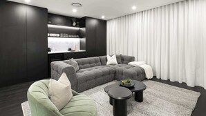 Ein modernes Wohnzimmer mit einem Ecksofa, einem grünen Sessel, einem Couchtisch und einer Küchenzeile mit Arbeitsplatte und Schränken.