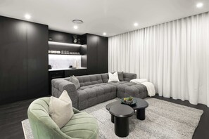 Ein modernes Wohnzimmer mit einem Ecksofa, einem grünen Sessel, einem Couchtisch und einer Küchenzeile mit Arbeitsplatte und Schränken.