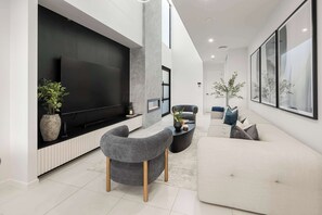 A modern living room with a large flat-screen TV, grey upholstered chairs, a white sofa, and a coffee table.