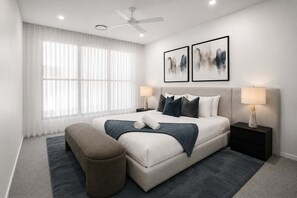 Ein modernes Schlafzimmer mit einem Bett, Nachttischen, einer Bank und Kunstwerken an der Wand.