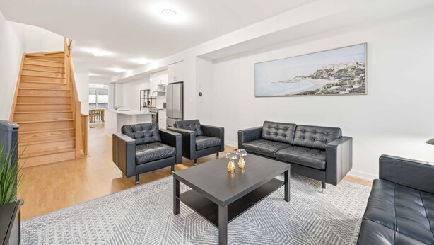 A modern living room with a staircase, a dining area, and a kitchen in the background.