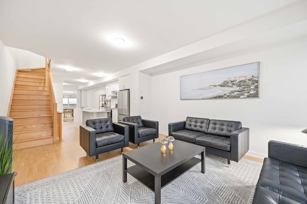 A modern living room with a staircase, a dining area, and a kitchen in the background.