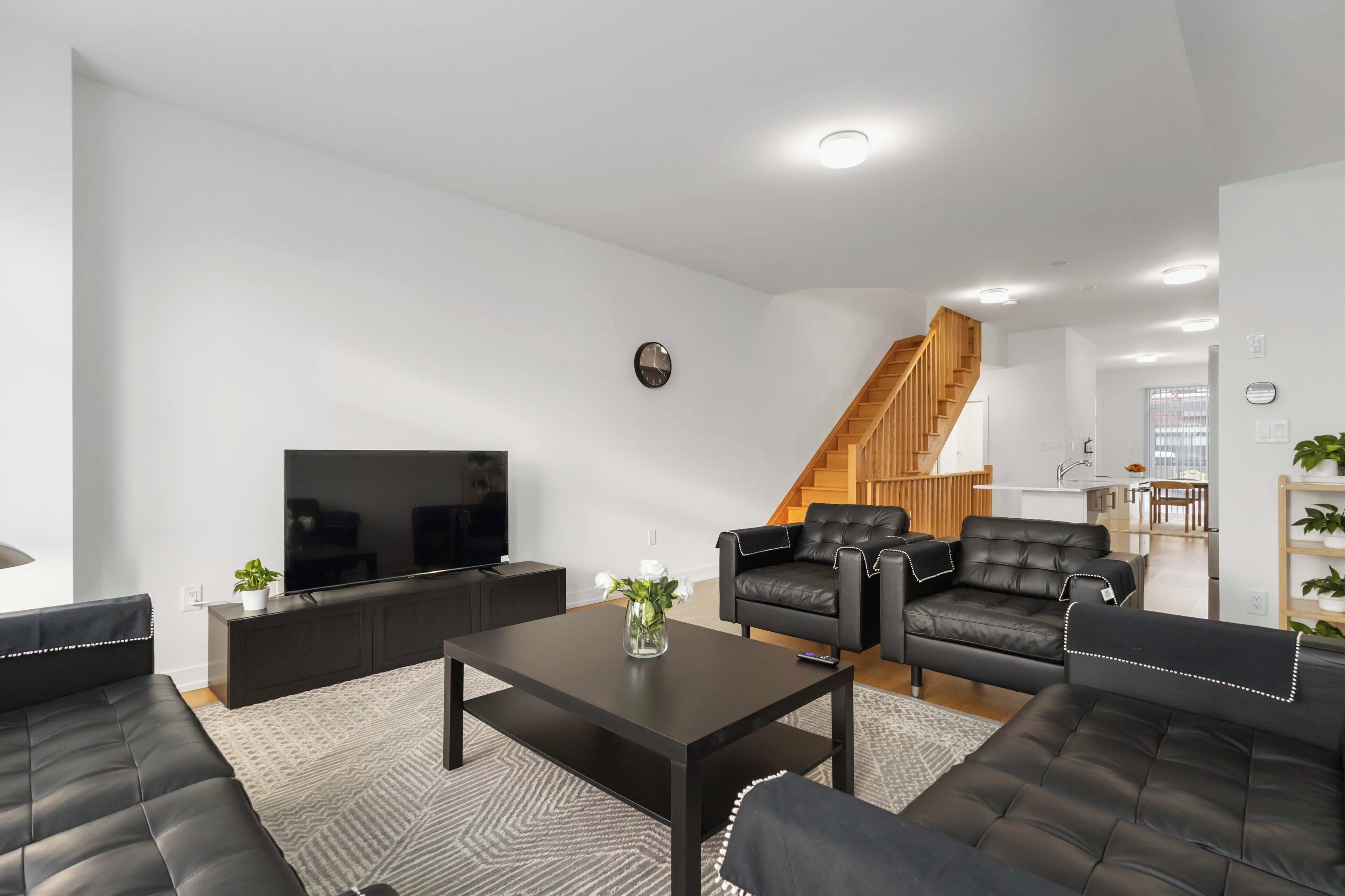 A modern living room with a flat-screen TV, leather sofas, a coffee table, and a staircase leading to an upper level.