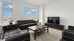 A modern living room with a black leather sofa, a coffee table, and a flat-screen TV.
