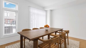 A dining area with a wooden table and chairs, a vase with flowers, and a window with blinds.