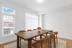 A dining area with a wooden table and chairs, a vase with flowers, and a window with blinds.