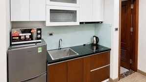 Una cocina compacta con armarios blancos, un refrigerador de acero inoxidable, una encimera negra y una puerta de madera.