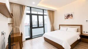 Habitación de hotel con una cama grande, televisión, balcón con cortinas y vistas a la ciudad.