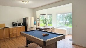Ett kök med ett biljardbord, ett kylskåp och ett fönster med utsikt över grönområden.