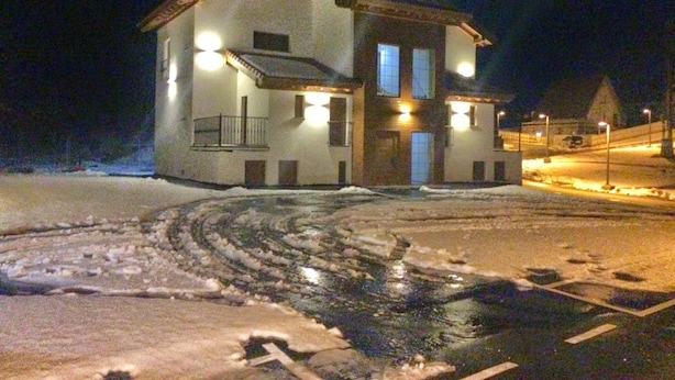 Een gebouw met twee verdiepingen en een balkon, verlicht door buitenverlichting, omgeven door sneeuw.