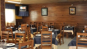 Een restaurant met meerdere tafels en stoelen, houten wanden en plafondverlichting.
