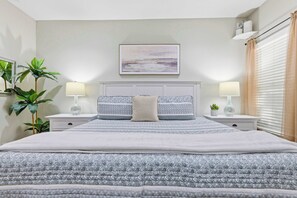 A neatly arranged bedroom with a bed, bedside tables, lamps, a painting, and a window with curtains. - "The Ultimate" 1.3 Acre! Guesthouse & Massive Pool! Pickleball & Putting Greens! (Gilbert)