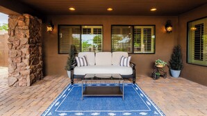 A covered patio area with a stone wall, a white sofa, a coffee table, and potted plants. - "The Ultimate" 1.3 Acre! Guesthouse & Massive Pool! Pickleball & Putting Greens! (Gilbert)