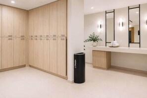 A hotel bathroom with wooden lockers, a trash bin, a sink with a mirror, and a potted plant. - Luxury 1BR Condo in Downtown Miami | Sleep 4  | Free Parking (Miami)
