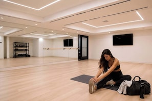 Een ruime kamer met houten vloer, een zwarte yogamat, een zwarte tas en een waterfles.