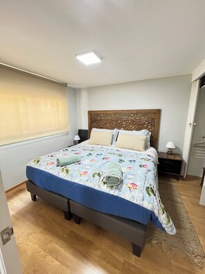 A bedroom with a bed, nightstands, a wooden headboard, a window with blinds, and a door. - 2-bedroom apartment in charming Las Condes with AC and comfort (Santiago)