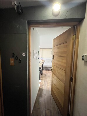 A hallway leading to a bedroom with a bed, a bedside table, and a lamp. There is a door with a number plate and a CENSO sign. - 2-bedroom apartment in charming Las Condes with AC and comfort (Santiago)