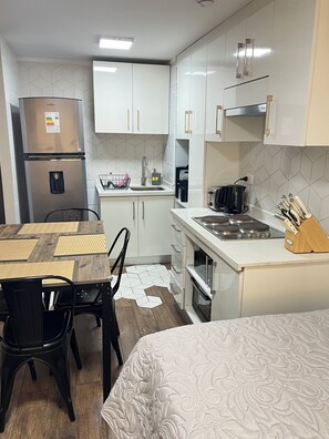 A compact kitchen with a refrigerator, sink, and stove. There is a dining table with chairs and a bed with a patterned bedspread. - 2-bedroom apartment in charming Las Condes with AC and comfort (Santiago)