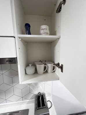 Eine Küche mit weißen Schränken, einer weißen Arbeitsplatte, einem Toaster und einem Regal mit einer Kaffeemaschine und einem Behälter mit dem Aufdruck 'HOME & FLOWERS'.