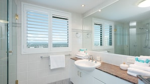 A modern bathroom with a large mirror, a glass shower enclosure, and a view through the window. - 3 Bedroom Skyview Sub Penthouse (Main Beach)