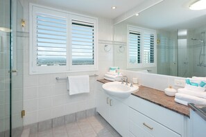 Ein modernes Badezimmer mit einem großen Spiegel, einer Glasdusche und Blick durch das Fenster.