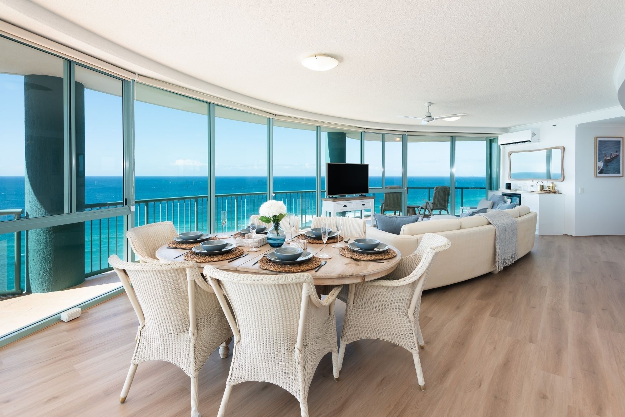 A spacious living area with a large window overlooking the ocean, a round dining table set with plates and glasses, and a comfortable seating arrangement.