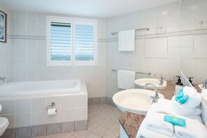 Une salle de bain moderne avec une baignoire, deux lavabos, une fenêtre et un porte-serviettes.