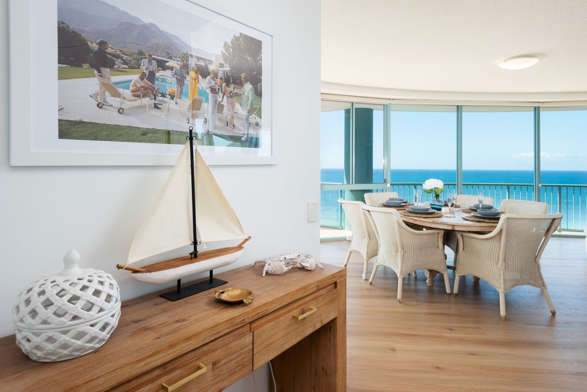 A dining area with a view of the ocean, a sailboat model, and a framed photograph on the wall.