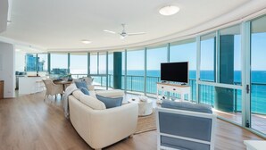 A spacious living area with a large window overlooking the ocean, a flat-screen TV, and a dining area with a view. - 3 Bedroom Skyview Sub Penthouse (Main Beach)