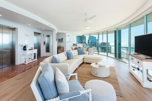 Ein modernes Wohnzimmer mit einem Ecksofa, einem Flachbildfernseher und einem großen Fenster mit Blick auf eine Stadtlandschaft.