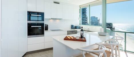 A modern kitchen with white cabinetry, a built-in oven, and a large window overlooking the ocean.