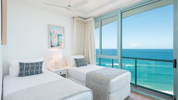 A hotel room with two beds, a ceiling fan, a large window with a view of the ocean, and a painting on the wall. - 3 Bedroom Skyview Sub Penthouse (Main Beach)