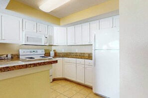 A kitchen with white cabinets, a microwave, a stove, and a refrigerator. - Carolinian Beach Resort 0833 (Myrtle Beach)