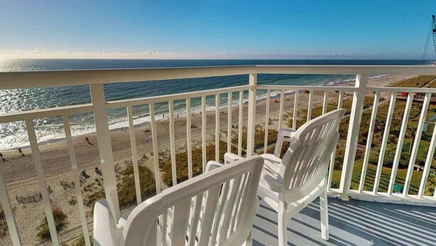 Varanda com cadeiras brancas com vista para a praia e oceano.
