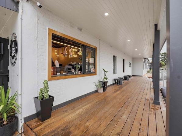Un café doté d’une terrasse en bois, de murs en briques blanches et de plantes en pot.