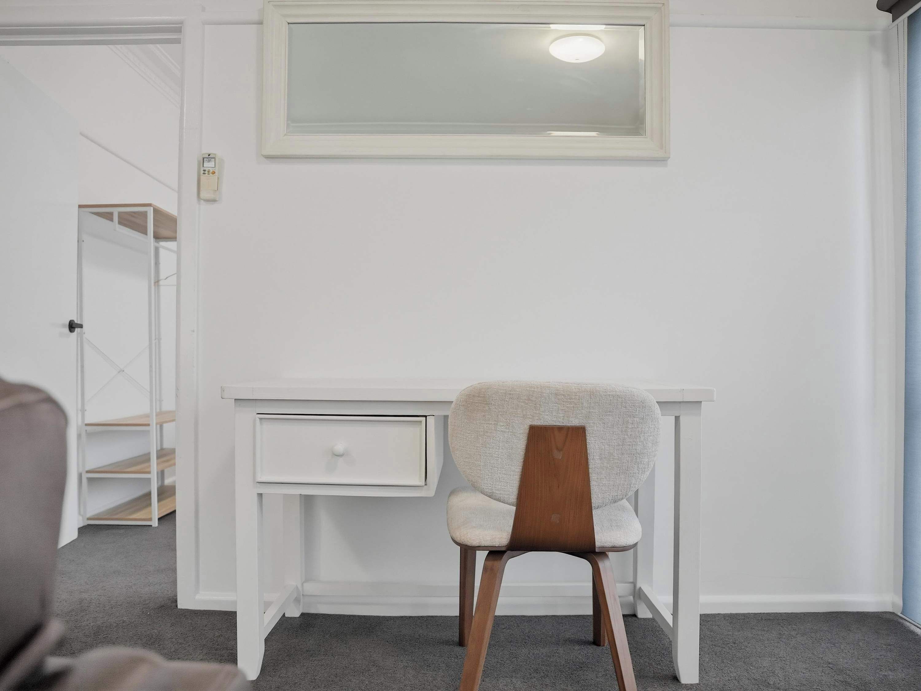 A white desk with a chair, a small shelf, and a wall-mounted light fixture.
