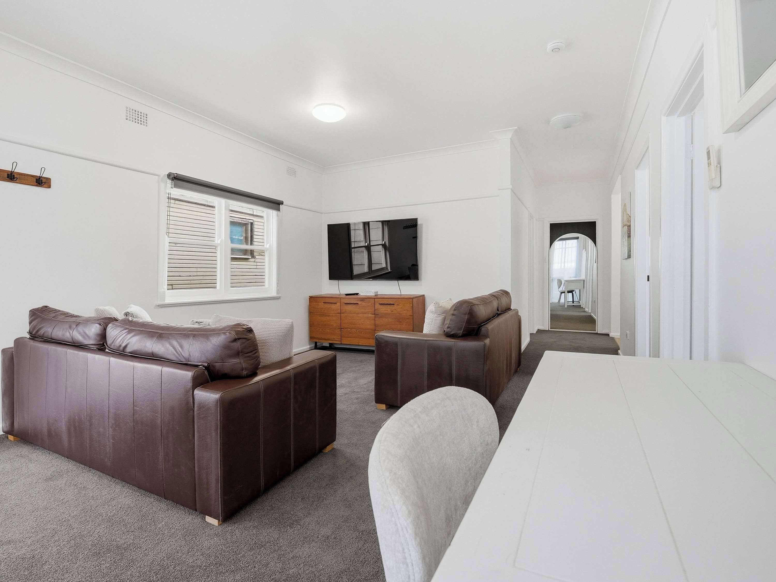 A modern living room with a sofa, a smaller seating area, a flat-screen TV, and a wooden cabinet.